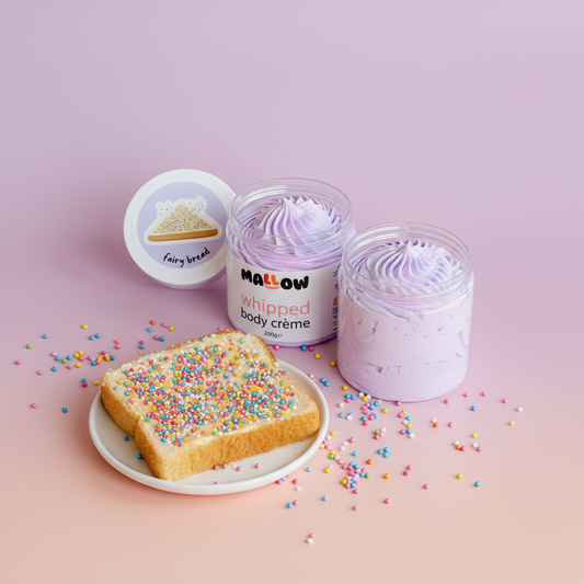Two containers of 'Mallow Whipped Body Crème' with a slice of toast and colorful sprinkles on a pink background.