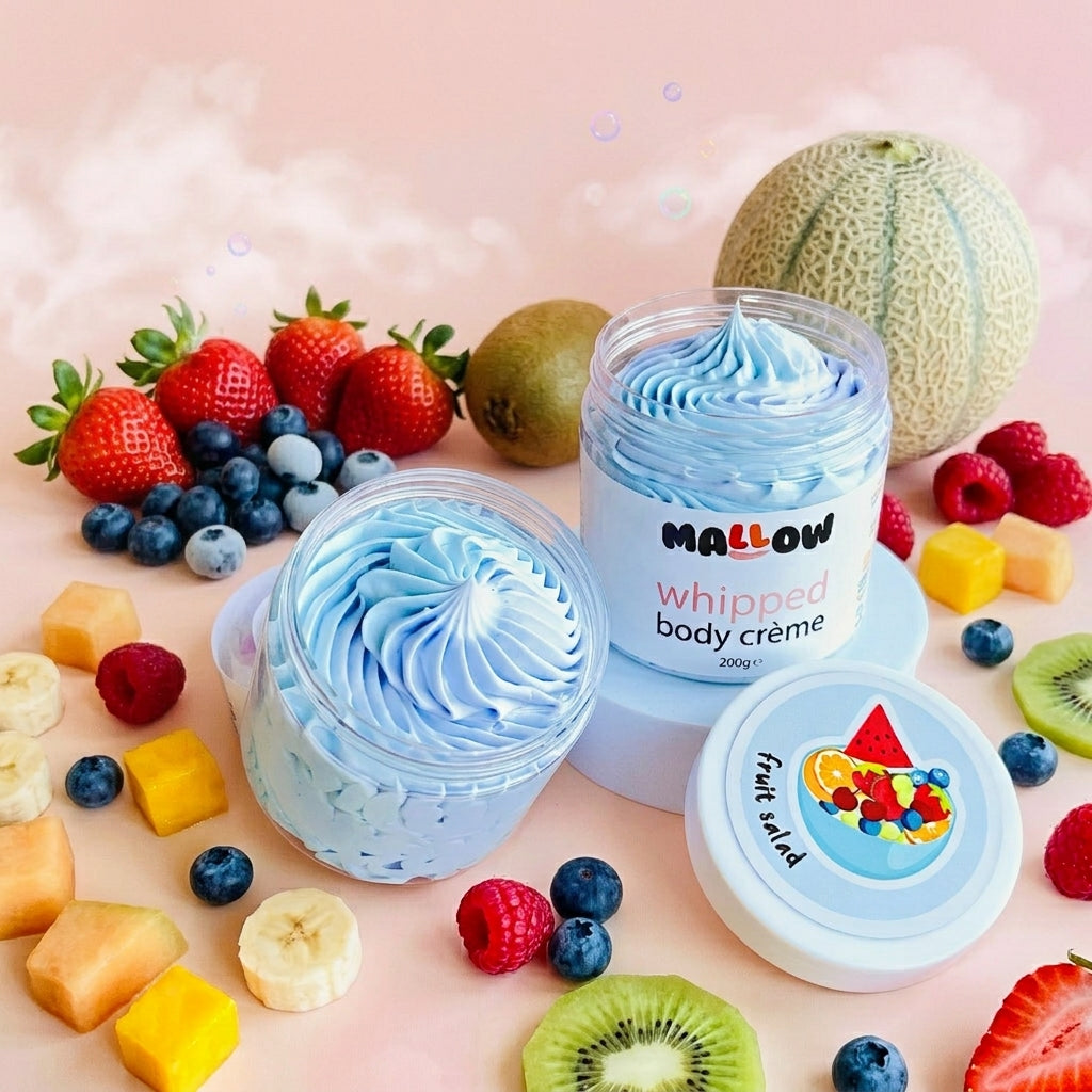 Two jars of Mallow whipped body creme in a light blue color, styled with fresh fruits like strawberries, blueberries, kiwi, and melon on a soft pink background.