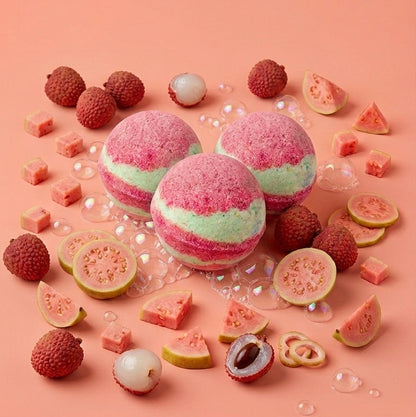 Three pink and mint green bath bombs arranged on a peach background, surrounded by sliced guava, lychee, and pink fruit pieces.