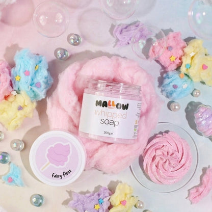 A styled flat-lay of a jar of Mallow Whipped Soap surrounded by cotton candy, pastel stars, bubble bubbles, and pearls on a pastel pink and blue background.